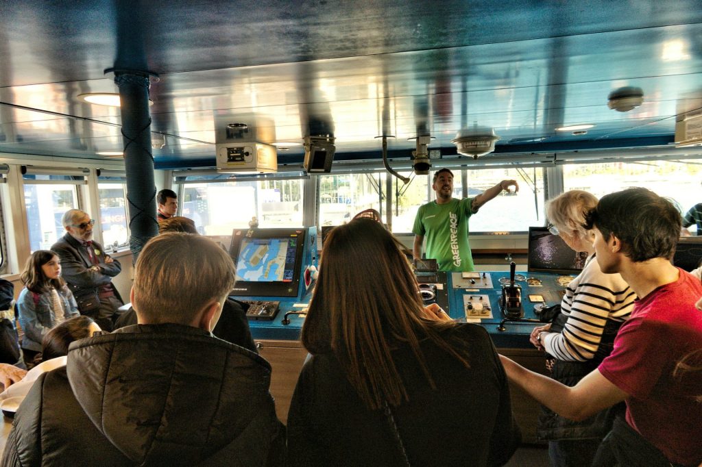 People gathered in a ship's bridge listening to a guide.